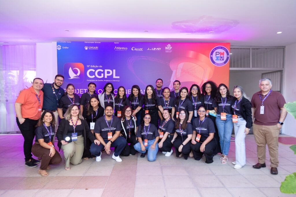 Foto em grupo da equipa de organizadores e voluntários do PMI Ceará sorrindo em frente ao painel da 15ª edição do CGPL.